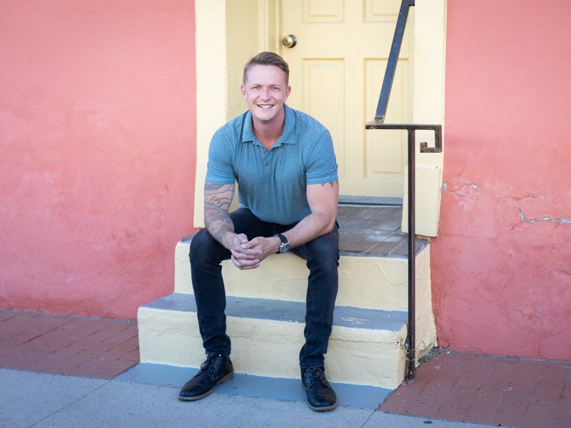 Dr. Tim Grivois, Executive Director wearing black pants and a blue polo shirt, seated on a staircase.